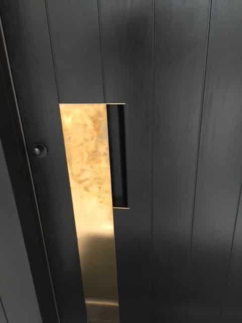 Vertical brass pull plate on a dark plank door